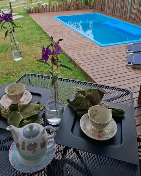 Uma mesa com xícaras e flores na varanda da frente, com o deck e a piscina ao fundo